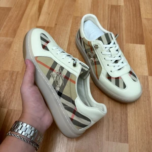 Burberry checkers sneaker  - Snygga sneakers från Burberry med klassiskt beige, svart och rött rutmönster. Skorna har vita skinnpaneler, snörning och en platt sula i gummi. Perfekta för dig som vill sticka ut med en lyxig och tidlös stil.