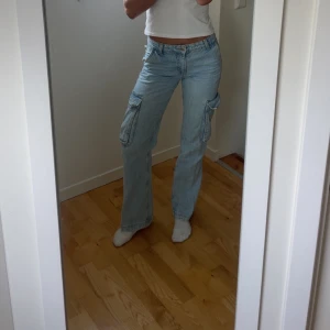 Ljusblå cargojeans med raka ben - Säljer ett par ljusblå cargojeans med raka ben och flera stora fickor på sidorna. Jeansen har normal. Perfekta för en avslappnad och trendig look.