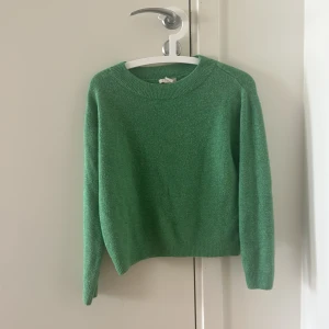 Grön stickad tröja med rund hals - En stilren grön stickad tröja med rund halsringning och långa ärmar. Perfekt för lager-på-lager och enkel att matcha med jeans eller kjol. Tröjan har en klassisk passform och ribbade muddar vid ärmslut och nederkant.