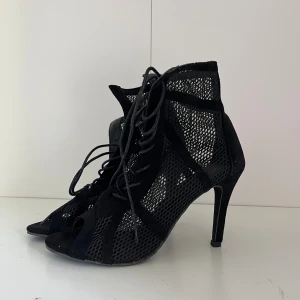 Svarta nätpumps med snörning och klack - Säljer ett par svarta pumps med höga klackar och coolt nätmaterial. Skorna har snörning framtill och öppen tå. Materialet är en mix av mocka och syntet med meshdetaljer perfekta för att dansa.