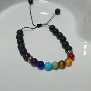 Färgglatt armband med lavastenar - Snyggt armband med svarta lavastenar och pärlor i regnbågens färger. Justerbar snörning gör att det passar de flesta handleder. Pärlorna är i lila, blå, turkos, grön, brun, gul och röd, vilket ger en cool och unik look.