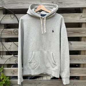 Ralph Lauren Grå Hoodie - Supersnygg hoodie från Ralph Lauren. Storlek M, skulle säga att den passar S Tröjan är i ett fint skick, enda ”defekten” är en färgförändring på sista bilden som inte syns så mycket irl (som ni kan se i bilden), ses även på mitten av tröjan i första bilden. Väldigt mjuk och härlig, inte använd mycket alls. Längden från axel och ner är 61,5 cm, och bredden från armhåla till armhåla är cirka 55 cm. Be gärna om fler mått. Hör gärna av er vid funderingar🙌🏻🙌🏻