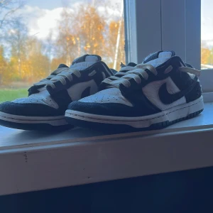 Nike Dunk Low svartvita sneakers - Nike Dunk Low sneakers i svart och vitt med klassisk Swoosh på sidorna. Ovandel i skinn och mocka, vita snören och svart yttersula. Perfekt för dig som gillar streetwear och vill ha en ikonisk look.väldigt fräsch kan tvättas upp och borsta med mocka borste innan jag skickar pris kan även diskuteras 