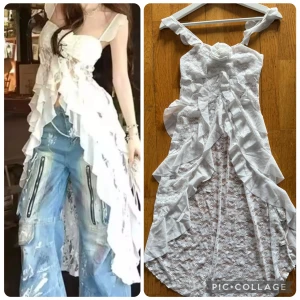 Vit spetsklänning med volanger och ros - Supersöt vit klänning i spets med volanger längs hela framsidan och en stor tygros vid bysten. Klänningen har smala axelband, omlottkänsla och är längre bak än fram. Perfekt för dig som gillar romantisk och unik stil.