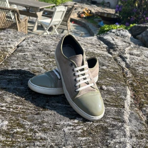 Lanvin sneakers i beige och olivgrön - Snygga sneakers från Lanvin med beige mocka på sidorna och olivgröna detaljer i skinn på tå och häl. Skorna har vita snören och en vit sula. Perfekta för dig som gillar stilrena och exklusiva sneakers med en twist.