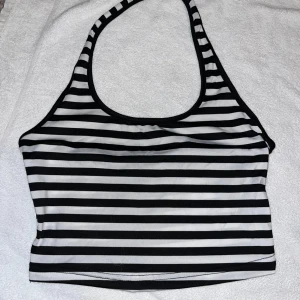 Randig svartvit croppad linnetopp - Säljer en croppad linnetopp med svarta och vita horisontella ränder. Toppen har halterneck och är ärmlös, perfekt för en chill och trendig look. Materialet känns mjukt och stretchigt, vilket gör den bekväm att bära hela dagen. Helt ny