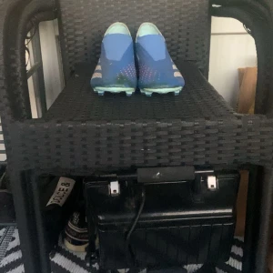 Blå adidas fotbollsskor utan snörning - Säljer ett par blå fotbollsskor från adidas med vita detaljer och klassiska tre ränder på sidorna. Skorna har en strömlinjeformad design och är tillverkade i syntetmaterial. Sulan är anpassad för spel på gräs (FG). Skorna är i storlek 45 1/3 men passar bra för 44 1/2 då jag använt de. Smutset kan rengöras vid tillfrågan😁