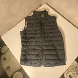 Parajumpers vest  - Snygg svart dunväst från Parajumpers med quiltad design och hög krage. Västen har dragkedja framtill, två sidofickor med dragkedja och en bröstficka. Insidan är ljusgrå och har klassiska Parajumpers-detaljer. Perfekt för lager-på-lager-stil. Om du är intresserad vänligen meddela 