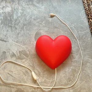 IKEA SMILA HJÄRTA Vägglampa - Charmig hjärtformad vägglampa från IKEA, modell SMILA HJÄRTA. Passar perfekt i barnrum eller som dekorativ belysning. Lampan har några ytliga repor men är i gott skick och fullt fungerande. Levereras med strömbrytare på sladden och E14-sockel för max 7W glödlampa.