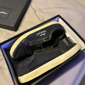 Svarta sneakers från Saint Laurent - Säljer mina svarta sneakers från Saint Laurent i storlek 43 utmärkt sick har andvänds sparsamt. Skorna har snörning, rund tå och platt sula i beige ton. Klassisk och stilren design som passar till streetwear och casual outfits och perfekt till hösten. Allt på bilderna medföljer!! Priset är ej hugget i sten 🪨 Tveka inte på att höra av vid frågor!! 💛✌️ 🍂 Alltid öppen för byten!