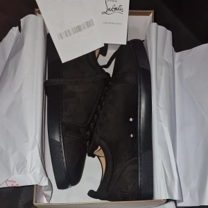 Christian Louboutin svarta mockasneakers - Svarta sneakers från Christian Louboutin i mjuk mocka med klassisk snörning och rund tå. Snygga svarta detaljer och ikonisk röd sula med Louboutin-logga. Perfekt för dig som vill ha en lyxig och stilren look med Paris-vibe. Storlek 43 passar till 42 