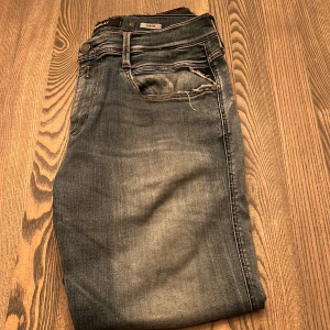 Replay Anbass jeans i tvättad blå - Snygga Replay Anbass jeans i tvättad blå denim med slitningar och klassiska fem fickor. Jeansen har en modern passform och detaljer som Replay-logga på myntfickan och bakficka med broderi. Perfekta för dig som gillar en avslappnad men trendig stil.