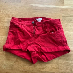 Röda denimshorts med uppvikt kant - Röda shorts i denim med klassisk femficksmodell och uppvikta benslut. De har bälteshällor, knapp och dragkedja framtill. 