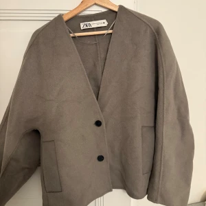 Grå kavaj från Zara med knappar - Snygg kort kappa från Zara i strl XS men är mer som S med två svarta knappar framtill och två fickor. Då den är lätt oversize passar de med en stickad tröja under. 