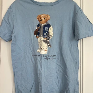 Blå Polo Bear t-shirt från Ralph Lauren - Snygg ljusblå t-shirt från Ralph Lauren med ikoniska Polo Bear-trycket på bröstet. 