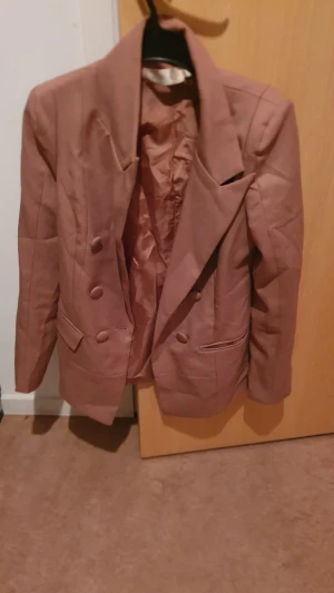 Kavaj - Snygg brun kavaj från H&M i storlek M. Dubbelknäppt med breda slag, två framfickor och matchande knappar. Materialet är slätt och kavajen har en klassisk, stilren look som passar perfekt till en cool outfit.