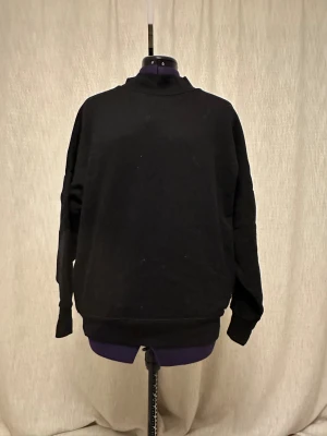 Svart sweatshirt från Calvin Klein Jeans - Svart sweatshirt från Calvin Klein Jeans med klassisk CK-logga vid kanten på högersidan. Tröjan har en enkel design med ribbade muddar och rundad hals. Tillverkad i mjuk bomull och har långärmad passform som är normal. Perfekt för en chill och stilren look.