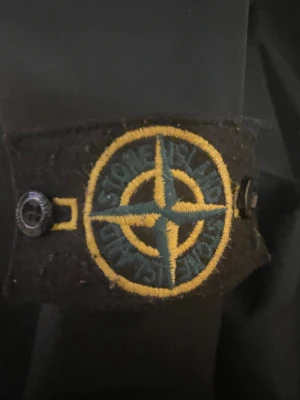 Svart vindjacka Stone Island S - Svart vindjacka från Stone Island i storlek S. Jackan har huva, dragkedja framtill och klassisk Stone Island patch på ärmen. Materialet är syntet och jackan har långa ärmar samt praktiska fickor med dragkedja. Perfekt för dig som gillar streetwear och snygga detaljer.Jag har haft på den typ 3-4 gånger nu jag vill bara sälja den och de är inget fel på ingen hål eller smutsiga saker på den