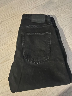 Svarta loose fit jeans Jack & Jones - Svarta jeans från Jack & Jones i modellen Loose/Chris. De har en loose passform med raka ben och klassisk femficksdesign. Jeansen är tillverkade i jeansmaterial och har en svart läderpatch bak i midjan. Perfekt för dig som gillar avslappnad stil.