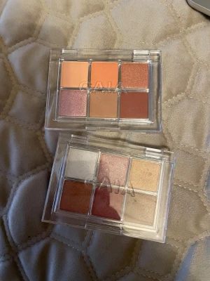 CAIA ögonskuggspaletter med varma toner - Två CAIA ögonskuggspaletter med sex nyanser vardera. Färgerna går i varma och neutrala toner som persika, koppar, beige, guld och rosé. Paletterna har både matta och skimrande skuggor, perfekt för att skapa snygga och trendiga ögonlooks. Genomskinlig plastförpackning med CAIA-logga.
