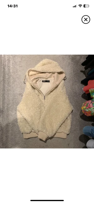 Beige teddyjacka med huva från Zara - Supermysig teddyjacka från Zara i beige med huva och dragkedja framtill. Jackan har ribbade muddar vid ärmslut och nederkant, samt en loose passform som ger en chill vibe. Perfekt för kalla dagar när du vill vara både varm och snygg. Orginal pris 700!
