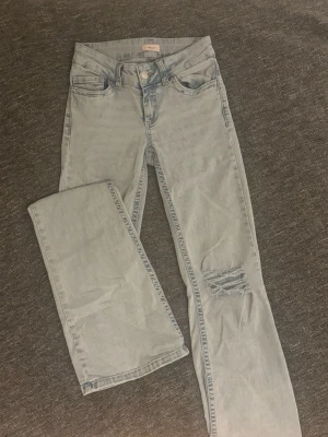 Ljusblå jeans med rosa brodyr från Nelly - Snygga ljusblå jeans från Nelly med rakt snitt och låg midja. Jeansen har en sliten detalj vid knät och cool rosa broderad zigzag på bakfickorna. Klassisk femficksmodell med knapp och dragkedja framtill. Perfekt för dig som gillar streetstyle.