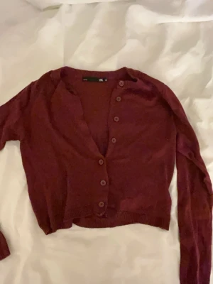 Vinröd croppad kofta - Snygg vinröd croppad kofta. Tröjan har ribbade muddar vid nederkant och ärmslut.