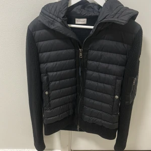 Svart jacka från Moncler - Svart jacka från Moncler med stickade ärmar. Perfekt för kyliga dagar och snygg streetstil. Den är i storlek M men passar bra som S också.Billigt!