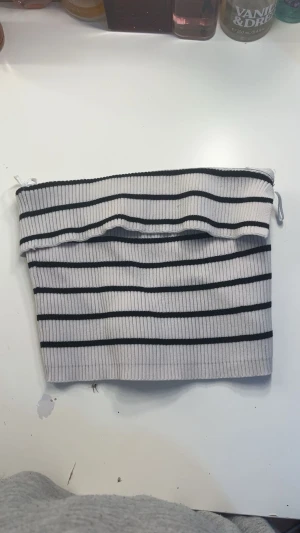 Randig bandeau tubtopp från FB Sister - Säljer en snygg bandeau tubtopp från FB Sister i storlek XXS. Toppen är vit med svarta horisontella ränder och har en ribbad, stickad struktur som ger en cool och modern vibe. Perfekt för dig som gillar minimalistisk stil med en twist.