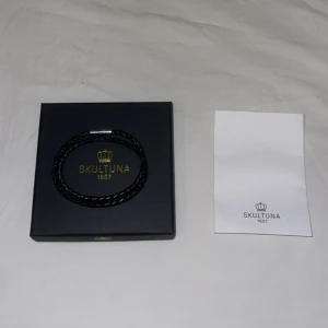 Svart flätat armband från Skultuna - Snyggt svart flätat armband från Skultuna med stilren silverfärgad magnetlås. Armbandet är gjort av skinn och har en modern, minimalistisk look som passar perfekt till din vardagsstil. Levereras i originalask med Skultuna-logga. Pris: 499kr | Ordnarie pris: 800kr