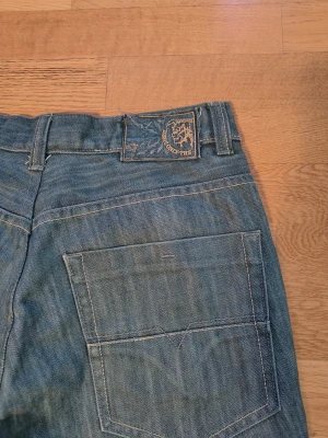 Blå jeans från Diesel Industry - Snygga blå jeans från Diesel Industry med klassisk femficksdesign och raka ben. Jeansen har ljus tvätt, kontrastsömmar och en tydlig Diesel-logga på myntfickan. Passar dig som gillar en enkel och stilren look.