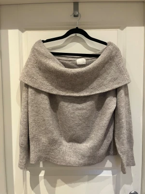 Beige offshoulder stickad tröja H&M - Supermysig beige stickad tröja från H&M i medium med bred offshoulder-krage. Perfekt för dig som gillar chill och stilren vibe. Tröjan har ribbade muddar och är långärmad, vilket gör den extra skön under kyliga dagar.