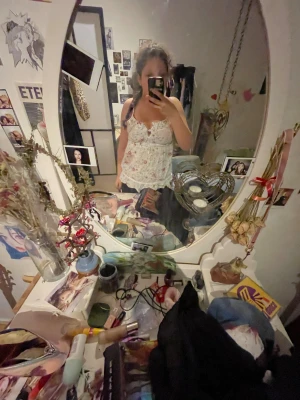 Blommig vit linnetopp med volang - Supersöt linnetopp i vit med blommigt mönster i rött och blått. Toppen har volangkant, spetsdetaljer och knyt i midjan. Den är ärmlös med smala axelband och har en v-ringad urringning. Perfekt för sommarens alla dagar!