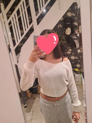 Vit croppad stickad tröja Kappahl - Snygg vit croppad stickad tröja från Kappahl med bred ribbad kant och v-ringad hals. Tröjan har långärmade ärmar och en offshoulder-look som ger en chill vibe. Perfekt för dig som gillar en enkel men trendig stil.