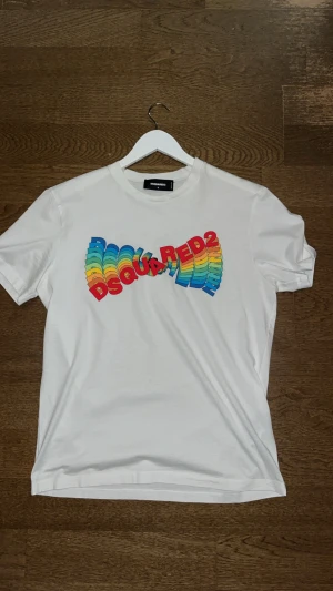Vit DSQUARED2 t-shirt med regnbågstryck i nyskick. - Säljer en vit t-shirt från DSQUARED2 i storlek S, tillverkad i mjuk bomull. Framsidan har ett färgstarkt regnbågstryck med DSQUARED2-loggan i 3D-effekt. Utmanande tröja för dig som vill sticka ut. Den är i nyskick och nypris ligger på 2000+. Storleken är S men sitter som M typ.