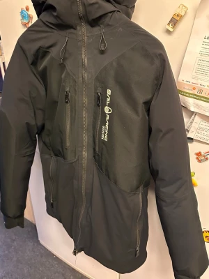 Sail Racing Vinterjacka - Säljer min Sail Racing-jacka. Den är använd och lite sliten, men fungerar fortfarande bra som vinterjacka och håller värmen utan problem.  Det enda felet: den övre zip-pullern (själva delen man drar i) har lossnat. Dragkedjan funkar, men du måste trycka upp den med tummen för att stänga den. Nedre delen fungerar som den ska.  Pris därför satt till 500 kr.  Bra jacka om du vill ha något varmt och funktionellt utan att lägga mycket pengar. 