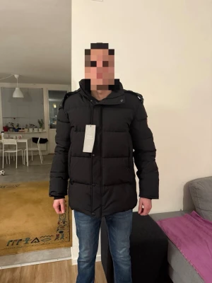 Svart dunjacka från Canada Goose - Säljer en svart dunjacka från Canada Goose med huva och pälskant. Jackan har klassisk patch på ärmen, raka linjer och dragkedja med knappar framtill. Perfekt för kalla dagar och riktigt snygg passform.