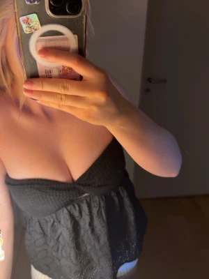 Svart  tubtopp  - Säljer en svart tubtopp med omlott-detalj över bysten och broderade blommor på den nedre delen. Toppen är axelbandslös och har en lätt volangkant nedtill!