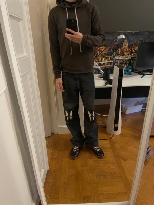 Our Legacy jeans med fjärilspatch - Unika svarta jeans från Our Legacy med breda ben och coola fjärilspatchar i svart och vitt på knäna. Klassisk femficksmodell med dragkedja och knapp, tillverkade i robust denim och detaljerade med kontrasterande material på knäpartiet. Patcharna är i läder. Den är använda dock mer sällsynta nu för tiden.