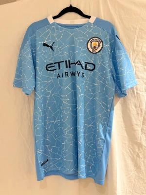 20/21  Manchester City De Bruyne tröja #17 - Manchester City matchtröja med De Bruyne 17 på ryggen. Ljusblå med vitt grafiskt mönster, officiellt klubbmärke och Puma-logga på bröstet. Tillverkad i lätt polyester med rund hals och korta ärmar. Snyggt tryck med Etihad Airways på framsidan.