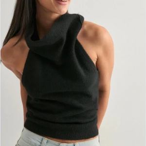 Svart stickad halterneck topp - Säljer en svart stickad halterneck topp med hög krage och öppen rygg. Toppen är ärmlös och har en tight passform som framhäver axlarna. Perfekt att styla med jeans eller kjol för en trendig look.
