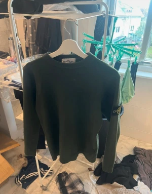 Mörkgrön Kashmir Stone Island tröja - Snygg mörkgrön stickad tröja från Stone Island med klassisk rund hals och långärmad passform. Tröjan har den ikoniska Stone Island patchen på vänster ärm och ribbade muddar vid ärmslut och nederkant. Perfekt för dig som gillar streetwear och vill ha något stilrent.