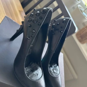 Svarta pumps med nitar från Scorett - Svarta pumps i äkta skinn från Scorett med spetsig tå och hög klack. Skorna har coola svarta nitar på hälen och baksidan som ger en edgy vibe. Perfekta för dig som vill sticka ut med detaljer och gillar en rockig stil.