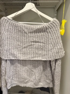 Grå offshoulder stickad tröja Gina Tricot - Säljer en grå stickad tröja från Gina Tricot med bred offshoulder-ringning. Tröjan har grovstickad struktur och långa ärmar, perfekt för dig som gillar en chill och trendig look. Passar dig som vill ha något mysigt men ändå snyggt.