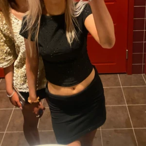 Svart tröja med öppen rygg😍 - Säljer en svart topp med små fina ”blommfigurer” till hål, för att få till det lilla extra. Toppen har korta ärmar och en tight passform som framhäver figuren. Öppen rygg för en snygg look. Perfekt för fest och till vardags! 🤩