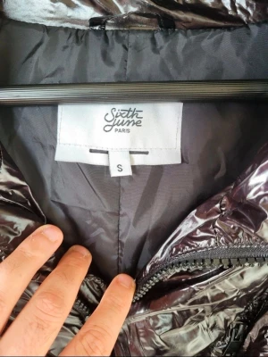 Svart pufferjacka från Sixth June S oversized  - Säljer en glansig svart pufferjacka från Sixth June Paris i storlek S. Jackan har hög krage, dragkedja framtill, snörning i midjan och på ärmarna samt flera fickor. Oversized passform och cool streetstil. Perfekt för kalla dagar när du vill sticka ut.