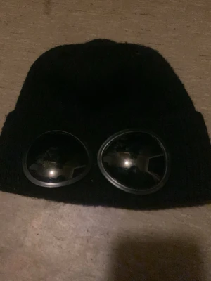 Svart mössa med inbyggd goggles - Säljer en riktigt cool svart mössa med fastsydda goggles framtill- perfekt för streetwear look,festival, cosplay eller bara när du vill sticka ut i mängden, mjuk och beskväm att bära samtidigt som den ger en unik och edgy stil.                                                                ✅one size, bra skick, passar båda tjejer och killar, ger outfiten det där lilla extra 