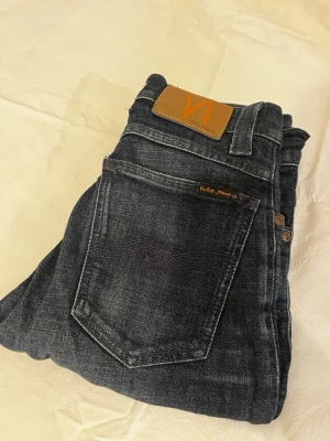 Svarta skinny jeans från Nudie Jeans - Snygga svarta jeans från Nudie Jeans i modellen skinny med klassisk femficksdesign och kopparfärgade nitar. Jeansen har en mörk tvätt med lätt slitning och är tillverkade i stretchig bomull för skön passform. Perfekt för dig som gillar en smal siluett.