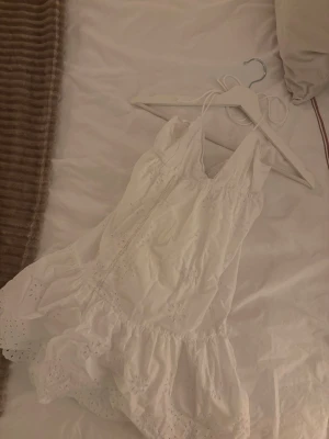 Vit kort sommarklänning med broderi - Superfin vit kort klänning från Zara med tunna axelband och v-ringning. Klänningen har broderade detaljer och volangkant nertill, vilket ger en romantisk och luftig känsla. Den är i storlek XS men skulle nog passa bättre som XXS🤍