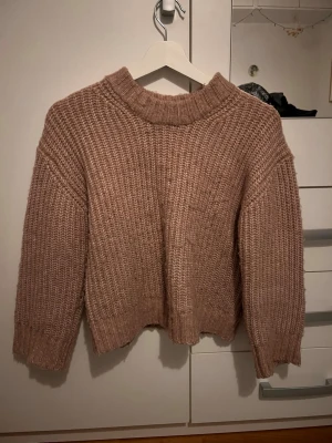 Beige stickad tröja från 157 - Mysig beige stickad tröja från 157 med grov ribbstickning och hög krage. Tröjan har en relaxed passform och långa ärmar, perfekt för kyliga dagar. Enkel att matcha med jeans eller kjol för en chill look.